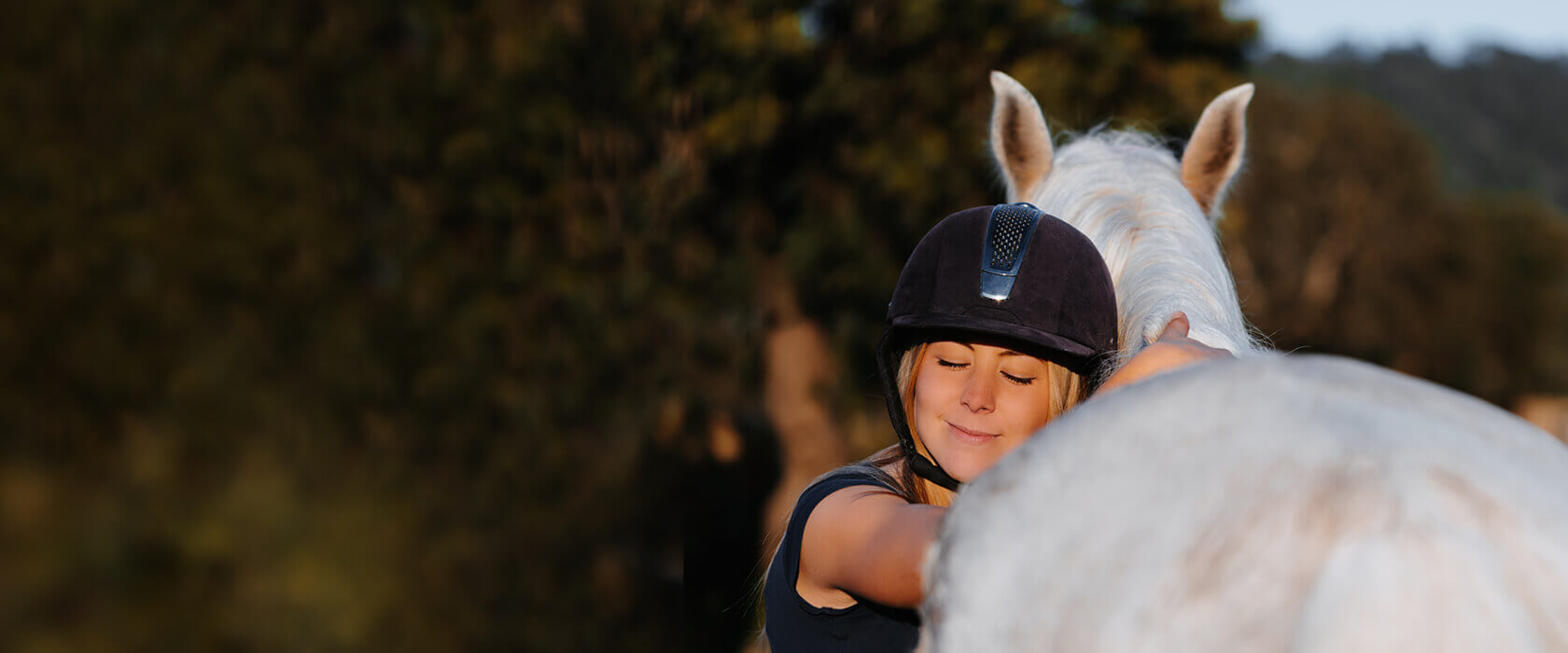 Mädchen mit Helm umarmt ein weißes Pferd