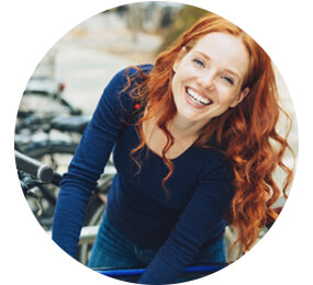 Lächelnde Frau steht vor Fahrrädern - Dank Fahrradversicherung gut abgesichert