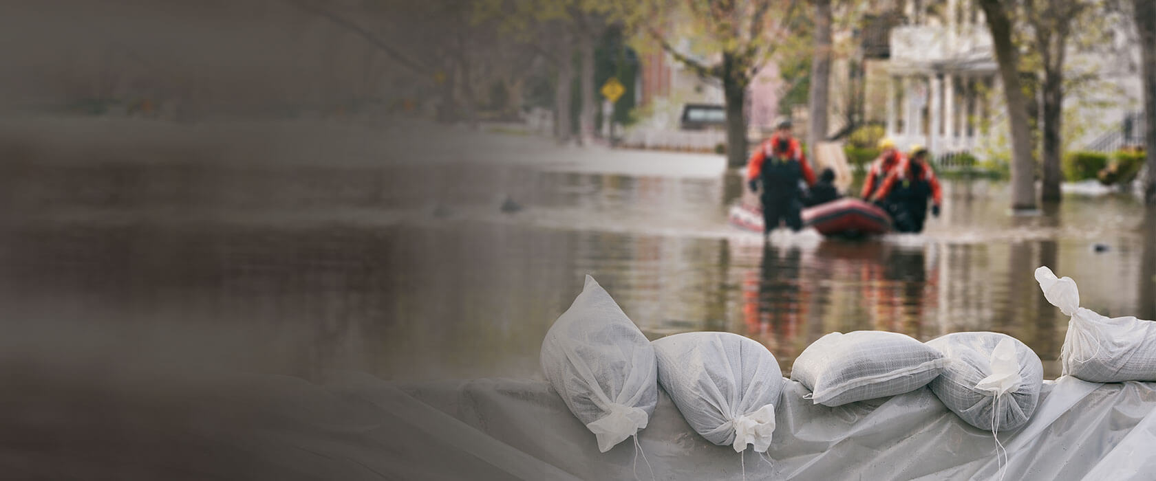 Symbolbild für Überschwemmung. Männer auf Boot vor Sandsäcken. Eine Elementarschadenversicherung schützt.