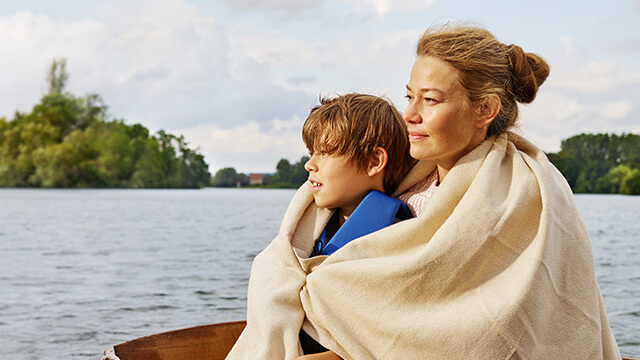 Ri­si­ko­le­bens­ver­si­che­rung der VGH: Mutter und Kind sitzen in Kuscheldecke  in einem Boot auf einem See 