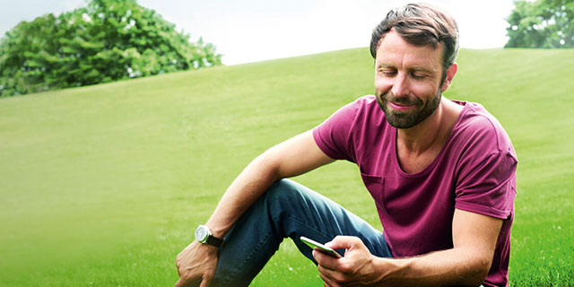 Mann informiert sich auf grüner Wiese sitzend über Gesundheit App für VGH-Kunden.