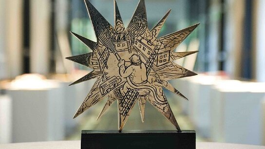 Dreidimensionale, sternförmige Skulptur mit künstlerischen Darstellungen von Menschen und Gebäuden im Hintergrund.