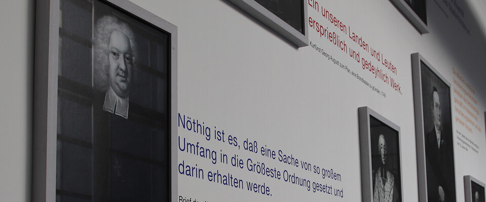 Porträts historischer Persönlichkeiten mit informativen Texten und Zitaten auf einer ausstellungsähnlichen Wand.