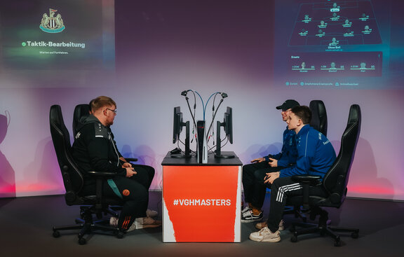 Finalpartie VGH Masters 2025 Finalpartie des Vorjahres. Zu sehen sind um einen Tisch mit Bildschirmen und Spielekonsolen rechts das Gewinnerduo Edwin Scheel und Timo Schiller. Ihnen gegenüber ihre zwei Finalgegner.