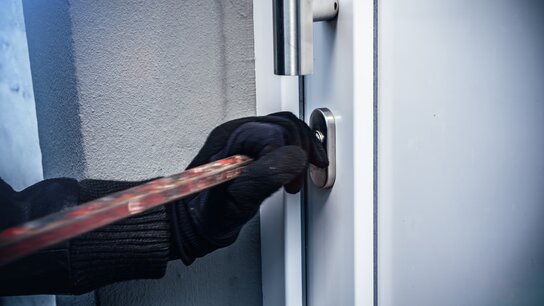 EineHand in schwarzer Handschuh hält einen Schraubenzieher, der in ein Türschloss eingeführt wird.