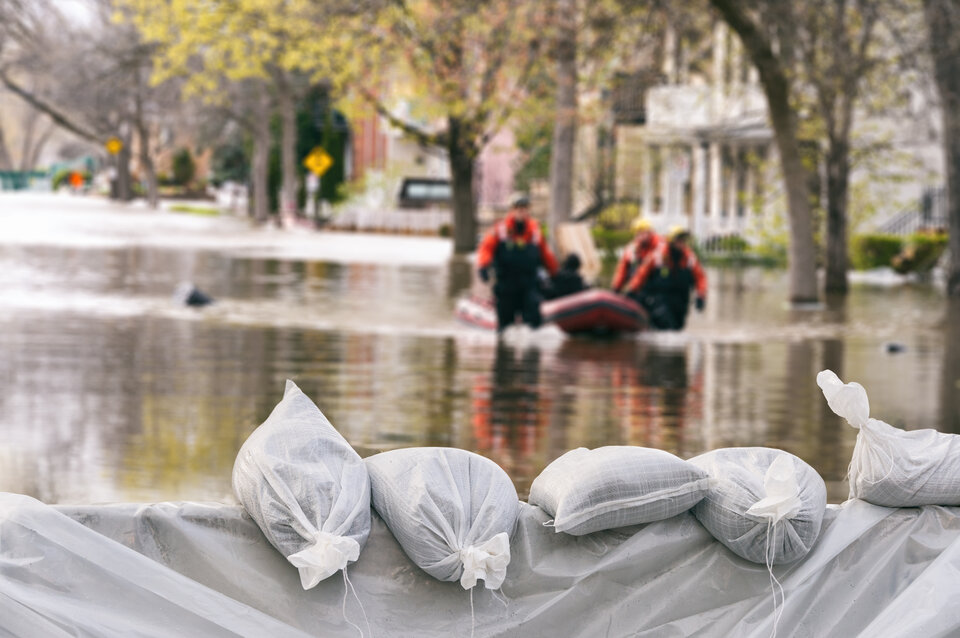 Sandbags schützen vor hochrangigem Wasser, während Rettungskräfte in einem Schlauchboot durch überflutete Straßen fahren.