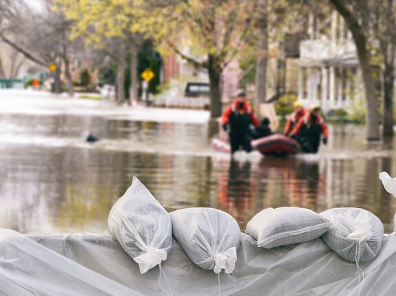 Sandbags schützen vor hochrangigem Wasser, während Rettungskräfte in einem Schlauchboot durch überflutete Straßen fahren.