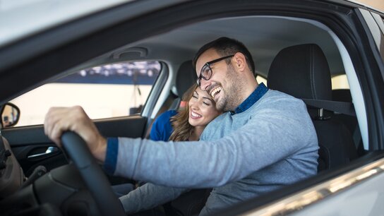 Ein Paar lächelt glücklich im Auto, während die Frau liebevoll an den Mann gelehnt ist.
